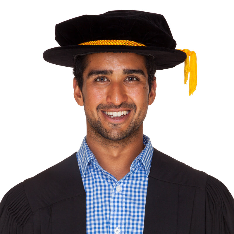 Man wearing a black velvet PhD Hat (bonnet) with a gold cord