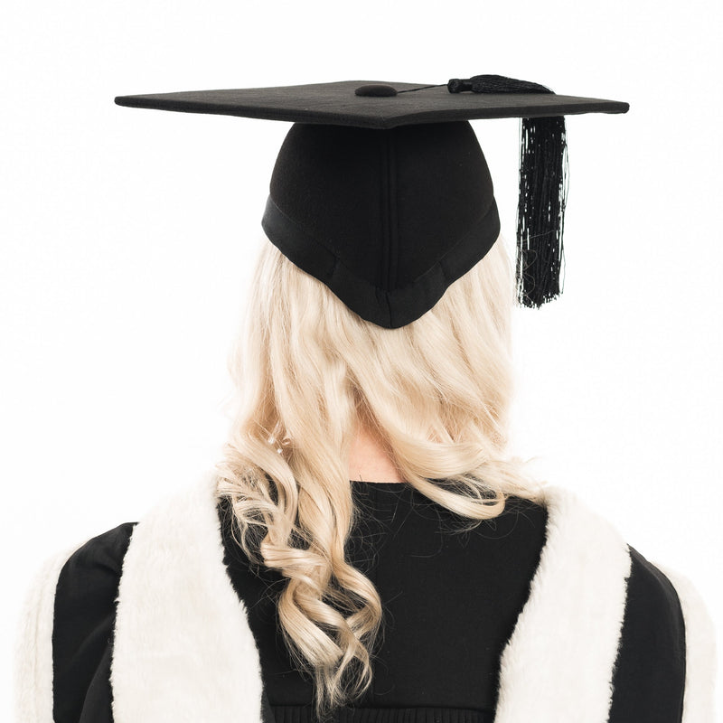 Woman from behind wearing a black felt graduation cap and graduation outfit